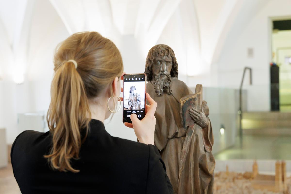 Frau fotografiert Apostelfigur mit einem Smartphone